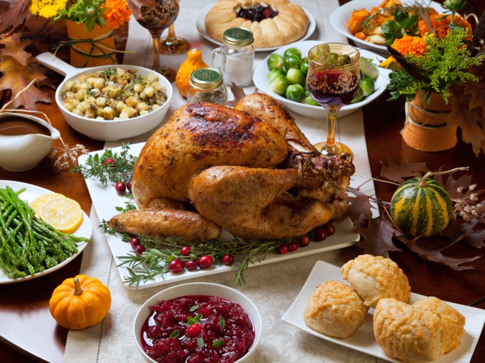 Roasted turkey garnished with cranberries on a rustic style table decoraded with pumpkins, gourds, asparagus, brussel sprouts, baked vegetables, pie, flowers, and candles.